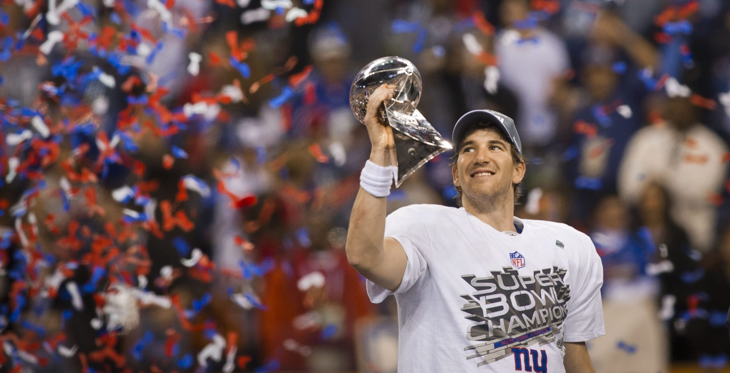New York Giants quarterback Eli Manning raises the Vince Lombardi Trophy amid falling confetti after winning the Super Bowl.